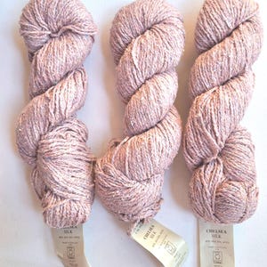 May include: Three skeins of Chelsea Silk yarn in a dusty pink hue with subtle flecks of color. Each skein features a paper label stating 65% silk and 35% wool, made in England, with a net weight of 3.5 ounces, and the brand name Tahki.