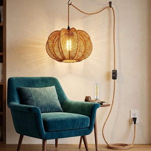 May include: A woven rattan pendant light hangs above a teal armchair. The light fixture is pumpkin-shaped and suspended by a rope cord. A small side table holds a decorative item and a lightbulb. The cord runs to a wall outlet.
