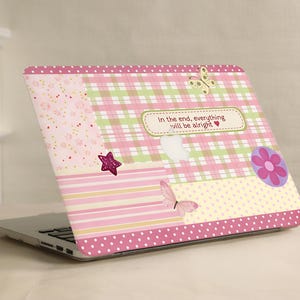 May include: Laptop with a decorative cover featuring a patchwork design in pink, green, and yellow. The cover includes a star, butterflies, and the text "In the end, everything will be alright". The design has a polka dot border.