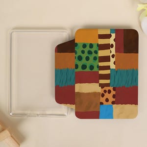 Peut inclure: Un étui de téléphone transparent et un étui de téléphone à motifs. L'étui à motifs présente un motif patchwork avec des carrés marron, verts, sarcelle et beige. Le motif comprend des pois et des rayures.