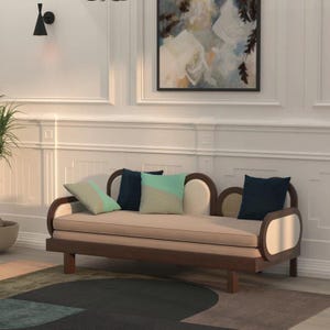 Può includere: Un divano letto con struttura in legno scuro dalle estremità arrotondate e rivestimento color beige chiaro. Il mobile include tre cuscini decorativi: uno piccolo verde chiaro e beige, uno blu scuro e uno più grande verde chiaro e beige.