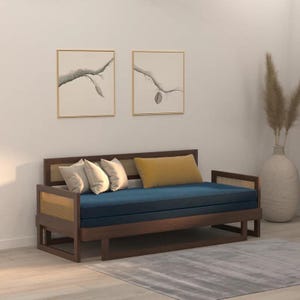 Può includere: Un divano letto con struttura in legno marrone scuro e pannelli laterali in paglia di Vienna naturale. Presenta un lungo cuscino di seduta blu profondo, tre cuscini bianchi e un cuscino lombare rettangolare color giallo senape.