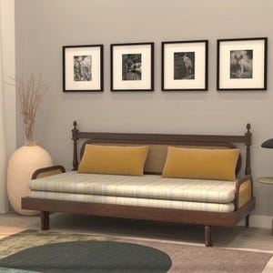 May include: A dark wood daybed featuring a woven cane backrest and side panels, topped with a light-colored plaid mattress cushion and two rectangular mustard yellow throw pillows, positioned against a wall with four framed black and white prints.