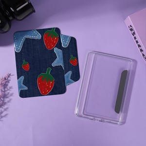 May include: A clear phone case and two denim-style cardholders with a strawberry and star pattern. The cardholders have a blue denim background with red strawberries and light blue stars.