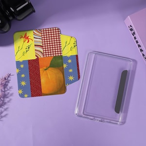 Peut inclure: Un ensemble de dessous de verre décoratifs avec un motif patchwork représentant une orange, des motifs floraux et un motif à carreaux rouges et blancs. Un étui rectangulaire transparent avec un accent noir est également présent.