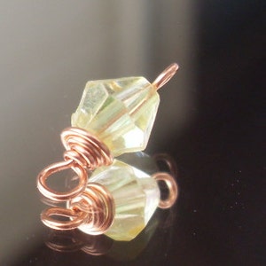 May include: A light green faceted glass bead with a copper wire wrap. The bead is attached to a copper wire loop.
