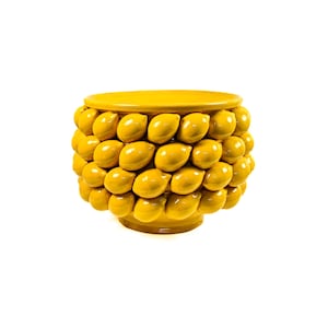 Può includere: Un vaso decorativo in ceramica giallo brillante con la parte superiore e la base rotonde. I lati del vaso sono adornati da un motivo di abbellimenti a forma di limone. Il vaso è posto su uno sfondo bianco.