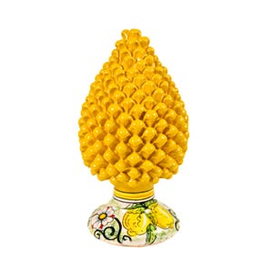 May include: A vibrant yellow ceramic pinecone ornament. The base is decorated with painted lemons, flowers, and green leaves. The pinecone has a textured surface composed of numerous small, rounded segments.