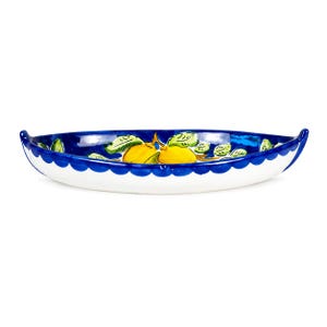May include: An elongated ceramic boat-shaped dish featuring a hand-painted design of bright yellow lemons and green leaves against a deep blue interior. The exterior is white with a scalloped blue rim and pointed, upturned ends on both sides.
