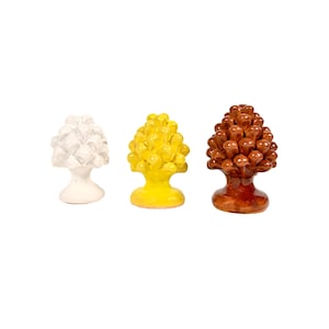 Può includere: Tre oggetti decorativi in ceramica a forma di pigna. Uno è bianco, uno è giallo e il terzo è marrone. Ognuno ha una superficie strutturata e una base, su sfondo bianco.