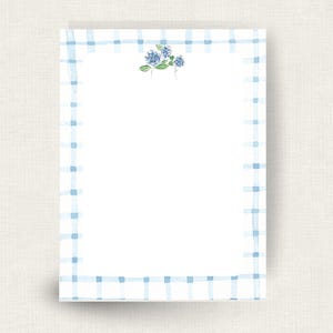 May include: A rectangular sheet of white stationery featuring a light blue watercolor plaid border. At the top center, there is a small, detailed watercolor illustration of blue hydrangea flowers with green leaves on thin stems.