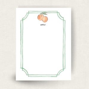 May include: A white rectangular notepad sheet featuring a hand-painted watercolor illustration of two peaches with green leaves at the top center. The word notes is printed in black below the fruit, framed by a double-lined sage green border.