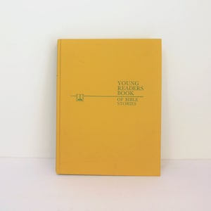 May include: A mustard-yellow book titled "Young Readers Book of Bible Stories" in green text. The book has a simple design with a horizontal line and a small graphic. The book is standing upright against a white background.