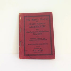 May include: A red book titled "The Master System of Short Method Arithmetic and Mechanical Calculations Simplified". The book is published by Joe Bond in Chicago, Illinois.