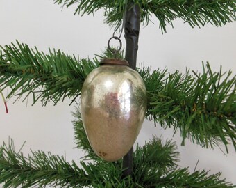 Puede incluir: Un adorno de Navidad de vidrio plateado con forma de huevo, colgado de un árbol de Navidad artificial verde.