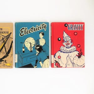 May include: Three vintage hardcover books with colorful illustrations. The first book is brown with the text "The Lighthouse" on the cover. The second book is blue with the text "Electricity" on the cover. The third book is red with the text "Gravity" on the cover.