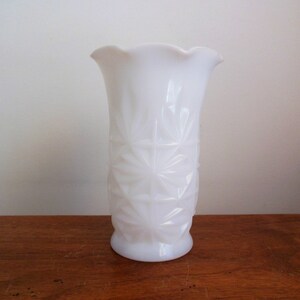 May include: A white milk glass vase with a diamond pattern. The vase has a scalloped rim and a slightly flared opening.