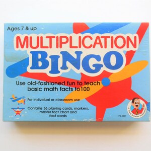 May include: A blue and red box with the words "Multiplication Bingo" in large, white letters. The box contains a game for ages 7 and up that uses old-fashioned fun to teach basic math facts to 100. It includes 36 playing cards, markers, a master fact chart, and fact cards.