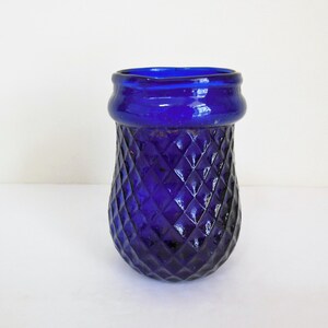 May include: A cobalt blue glass vase with a diamond pattern. The vase has a wide mouth and a rounded bottom.