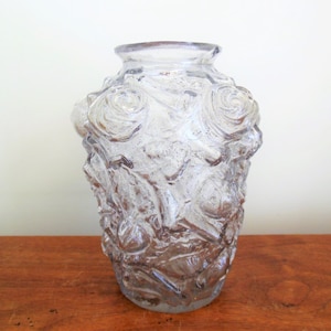 May include: A clear glass vase with a textured surface featuring raised rose designs. The vase has a rounded body and a slightly flared opening.