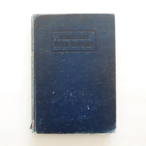 May include: A vintage blue book titled "Elementary Bible History." The book has a worn cover with the title embossed in a rectangular frame. The edges show signs of wear and tear, suggesting age.