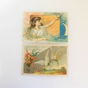 May include: Two vintage Easter greeting cards. The top card features a young girl in a white dress reaching out to a white dove flying over a blue crescent moon. The bottom card features a bouquet of yellow and pink flowers with two white doves flying above. The text on the bottom card reads "The Woolson Spice Co's Easter Greeting."