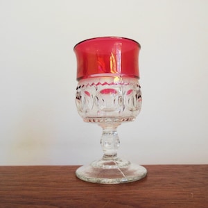 May include: A clear glass goblet with a red glass rim. The goblet has a textured pattern of small circles around the bowl and stem.