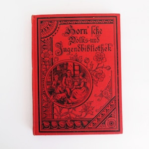 May include: A red book cover with black lettering that reads "Born'sche Volks- und Jugendbibliothek". The cover features a decorative border with floral designs and a circular illustration of a family gathered around a table.