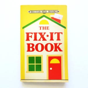 May include: A vintage book titled "The Fix-It Book" with a house-shaped design. The cover is yellow with a green roof, red door, and green window. The text is in red and the book is from "Better Way Books".