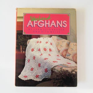 May include: A book titled "Weekend Afghans" by Jean Leinhauser and Rita Weiss. The cover features a white crocheted afghan with pink flowers on a couch.