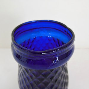 May include: A cobalt blue glass vase with a diamond pattern. The vase has a wide mouth and a narrow base.