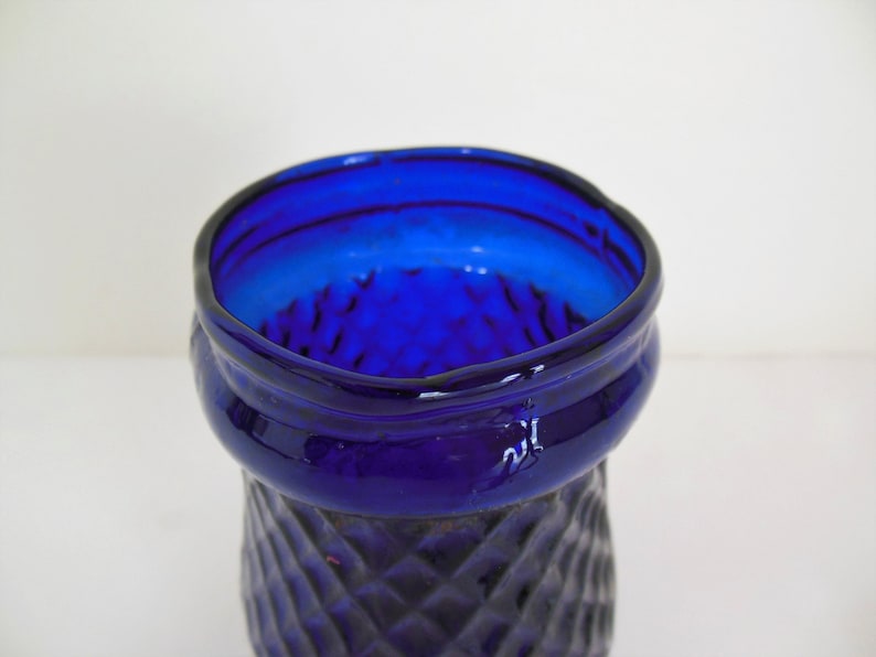 May include: A cobalt blue glass vase with a diamond pattern. The vase has a wide mouth and a narrow base.