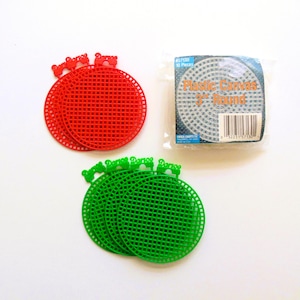 May include: A set of red and green round plastic canvas pieces with a grid pattern and a tab at the top. A sealed package labeled Plastic Canvas 3" Round contains ten pieces, with the text Darice visible on each individual plastic canvas piece.