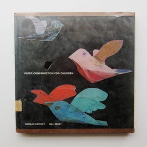 May include: Vintage book cover with a dark background and colorful paper bird illustrations. The title "PAPER CONSTRUCTION FOR CHILDREN" is printed in white, with the authors' names below. The cover has a worn appearance.