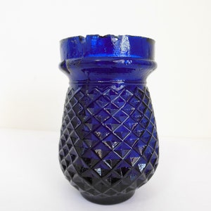 May include: A cobalt blue glass vase with a diamond pattern. The vase has a wide mouth and a rounded base.
