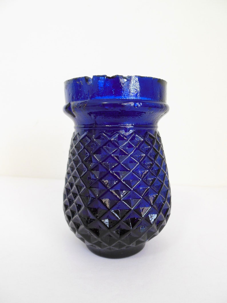 May include: A cobalt blue glass vase with a diamond pattern. The vase has a wide mouth and a rounded base.