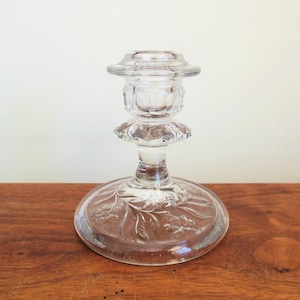May include: A clear glass candlestick with a fluted design and a floral pattern on the base.