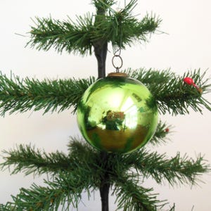 May include: A shiny green glass Christmas ornament hanging on a green artificial Christmas tree.