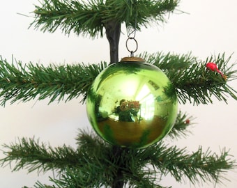 Puede incluir: Un adorno de Navidad de vidrio verde brillante colgado de un árbol de Navidad artificial verde.