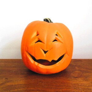 May include: A carved orange pumpkin with a smiling face. The pumpkin is sitting on a wooden surface.