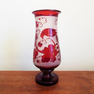 May include: A red glass vase with a white frosted design of birds and leaves. The vase has a flared base and a round top.