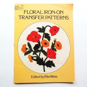 May include: A softcover book titled Floral Iron-On Transfer Patterns edited by Rita Weiss. The yellow cover features a central circular illustration of red and orange flowers with dark green leaves from the Dover Needlework Series collection.