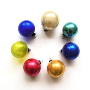 May include: Seven vintage glass Christmas ornaments in various colors, including blue, green, gold, red, and white. The ornaments are arranged in a circle on a white background.