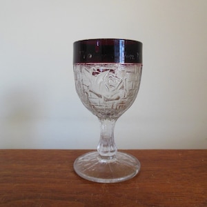May include: A clear glass goblet with a deep purple rim and a rose etched design. The rim is inscribed with the text "World's Columbian Exposition 1893".