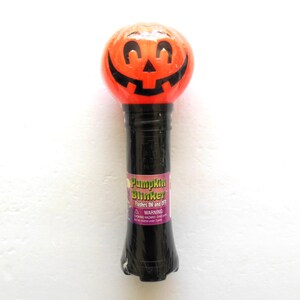 May include: A Halloween-themed Pumpkin Blinker toy. The top is a round, orange pumpkin face with black features. The black handle has a label that reads "Pumpkin Blinker" and "Flashes ON and OFF".