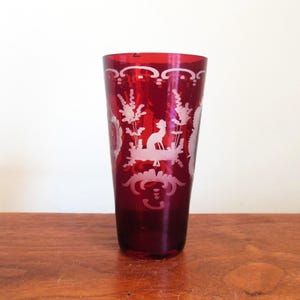 May include: A tall, clear glass vase with a red, opaque base. The vase is decorated with a white, etched design of a bird and floral motifs.