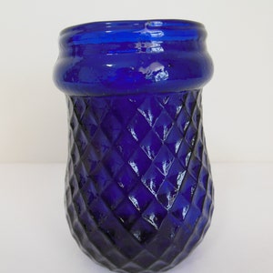 May include: A cobalt blue glass vase with a diamond pattern. The vase has a wide mouth and a rounded bottom.