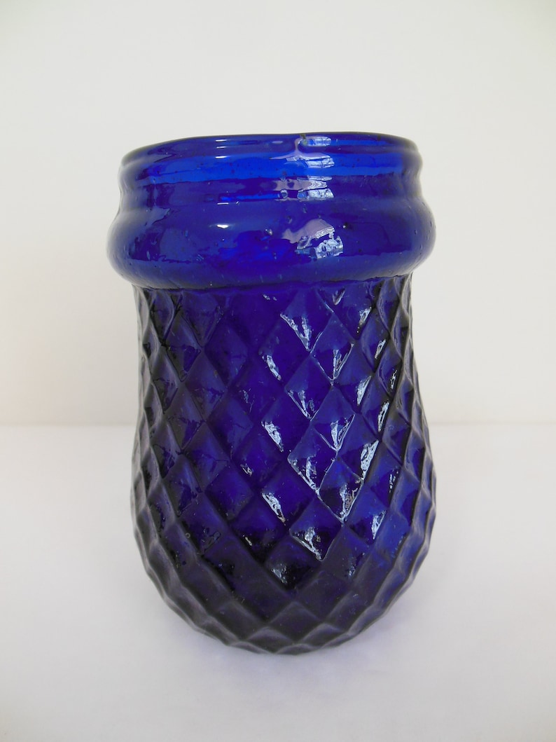 May include: A cobalt blue glass vase with a diamond pattern. The vase has a wide mouth and a rounded bottom.