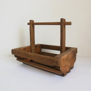 May include: A rustic wooden basket with a carrying handle. The basket is made of natural wood and has a weathered brown finish.