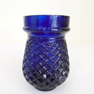 May include: A cobalt blue glass vase with a diamond pattern. The vase has a wide mouth and a rounded base.
